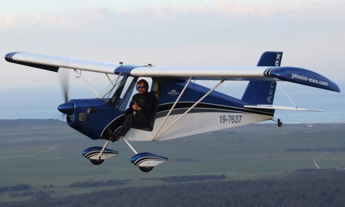 A blue and white AeroMax in flight, seen from above against a hazy landscape