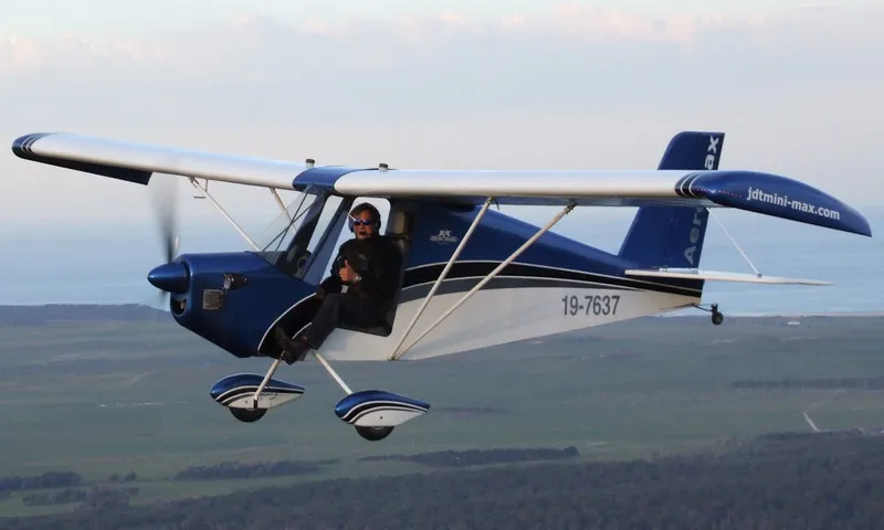 A blue and white AeroMax in flight, seen from above against a hazy landscape