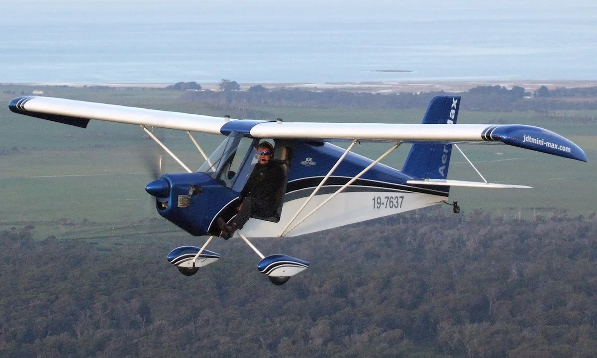 A blue and white AeroMax low-wing aircraft in flight over farmland