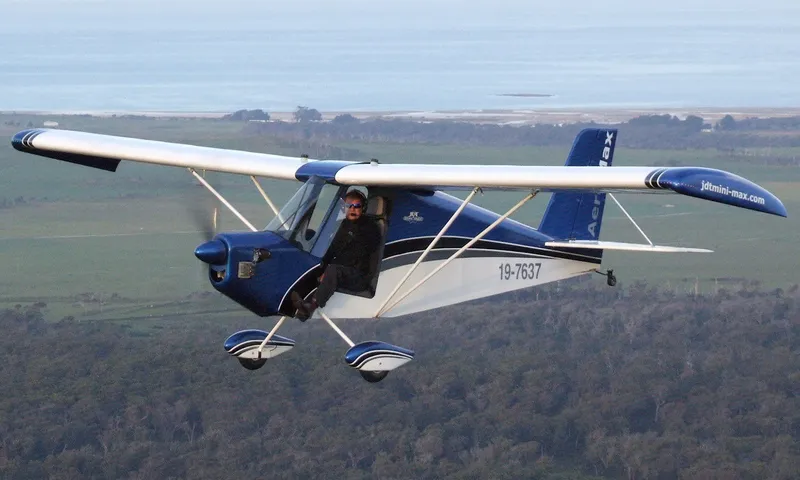 A blue and white AeroMax low-wing aircraft in flight over farmland