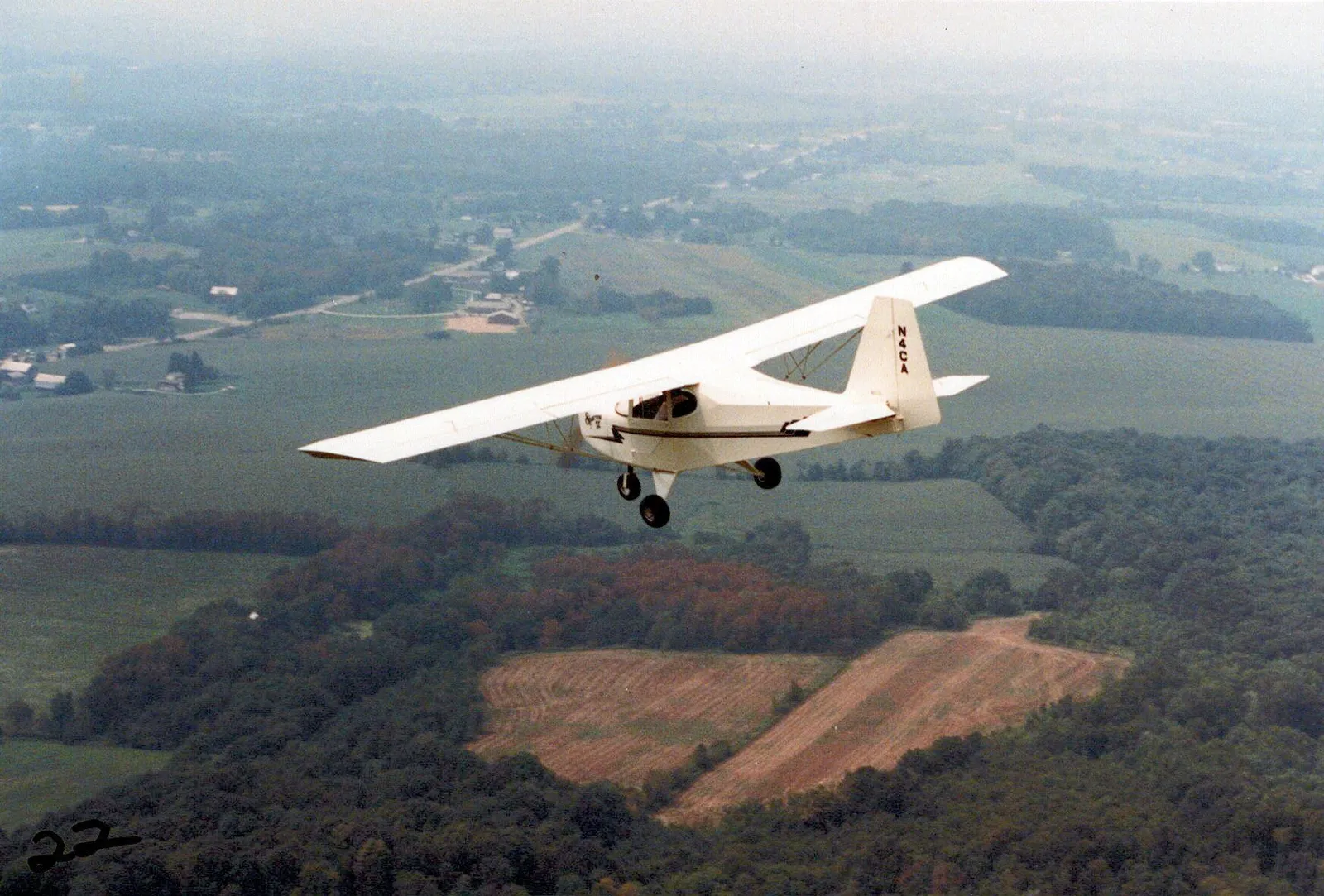 A Carlson Sparrow II in flight over farmland and woods