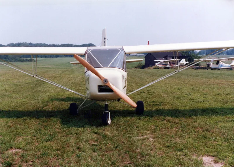 A white Carlson Sparrow II seen head-on on a grass airfield, propeller stopped