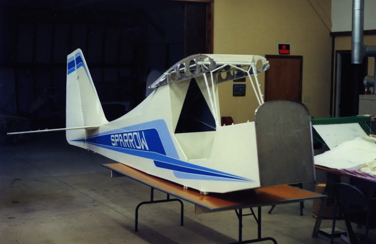 An uncovered Carlson Sparrow fuselage and tail with the wing structure exposed, in a shop