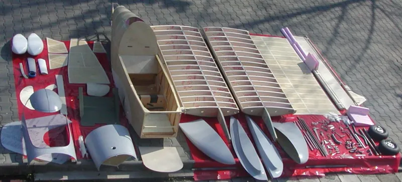 An SD-1 kit laid out on a red sheet: plywood-covered fuselage, two wing structures with ribs, moulded parts, control surfaces, wheels and hardware