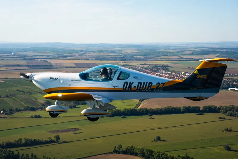 A silver and orange two-seat Spacek SD-2 SportMaster in flight over farmland